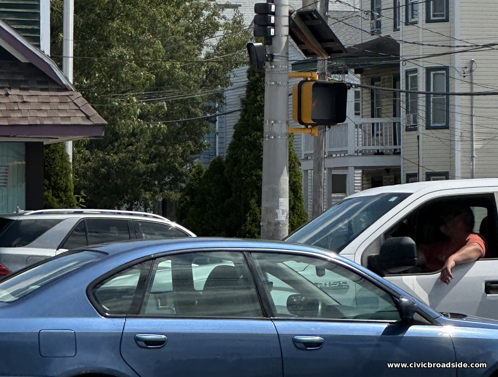 A Flock Safety camera mounted on a traffic signal pole above a Malden street, partially obscured among traffic lights and utility wires