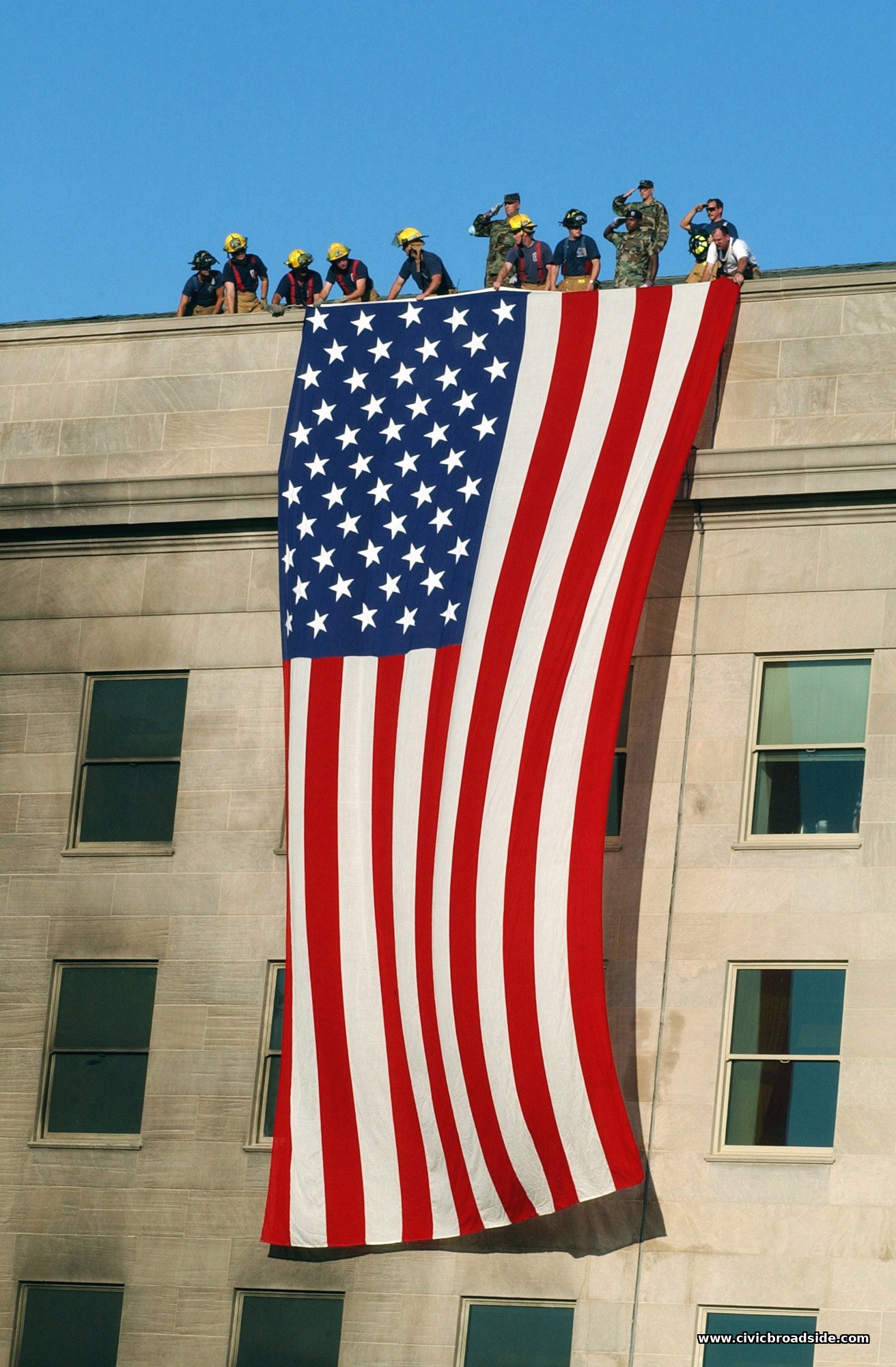 Soldiers from the 3rd Infantry render honors as firefighters and rescue workers unfurl a large American flag down the face of the Pentagon