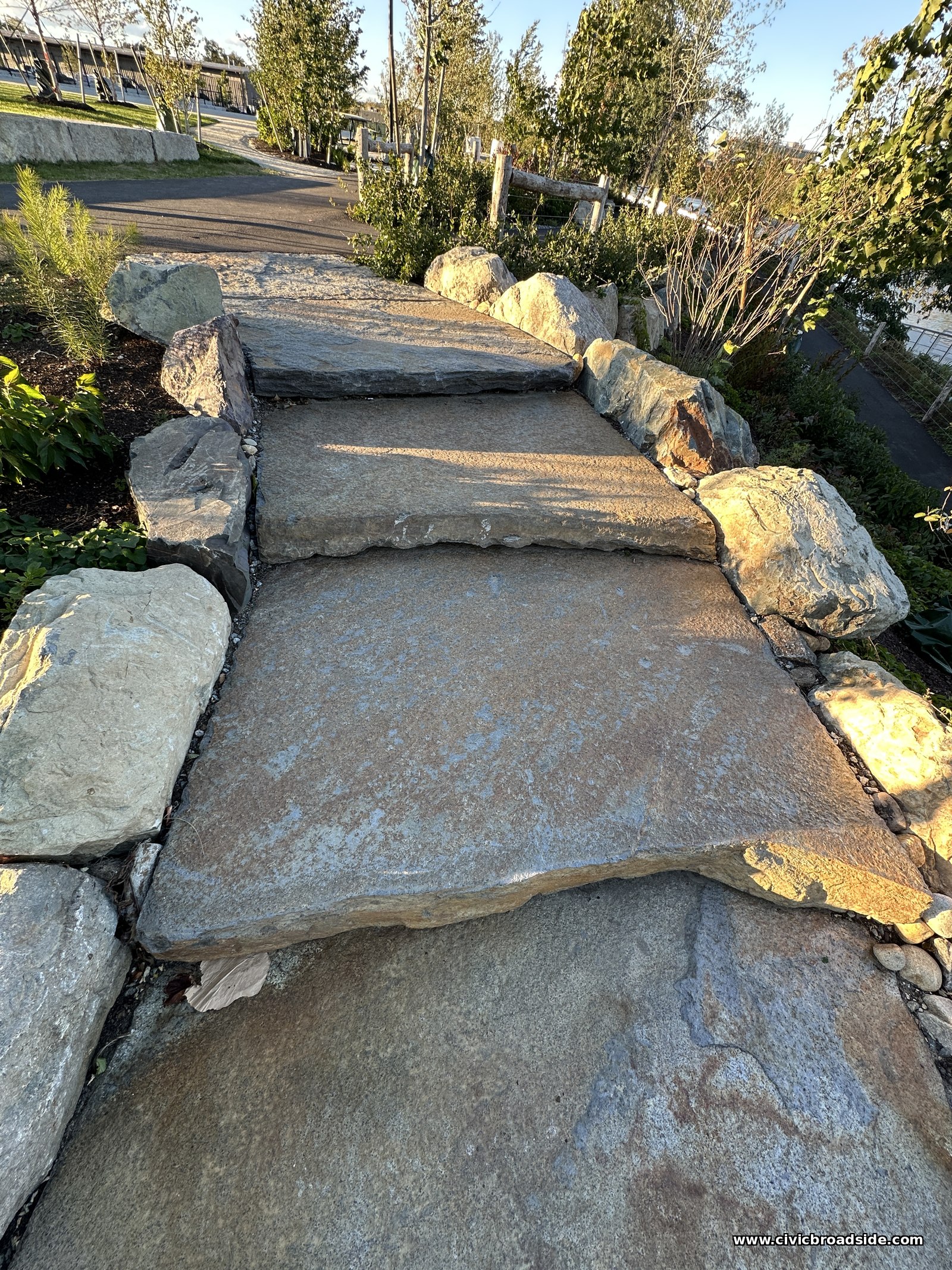 A close view of three stone slab treads of different depths and thicknesses, bordered by boulders, with no railing