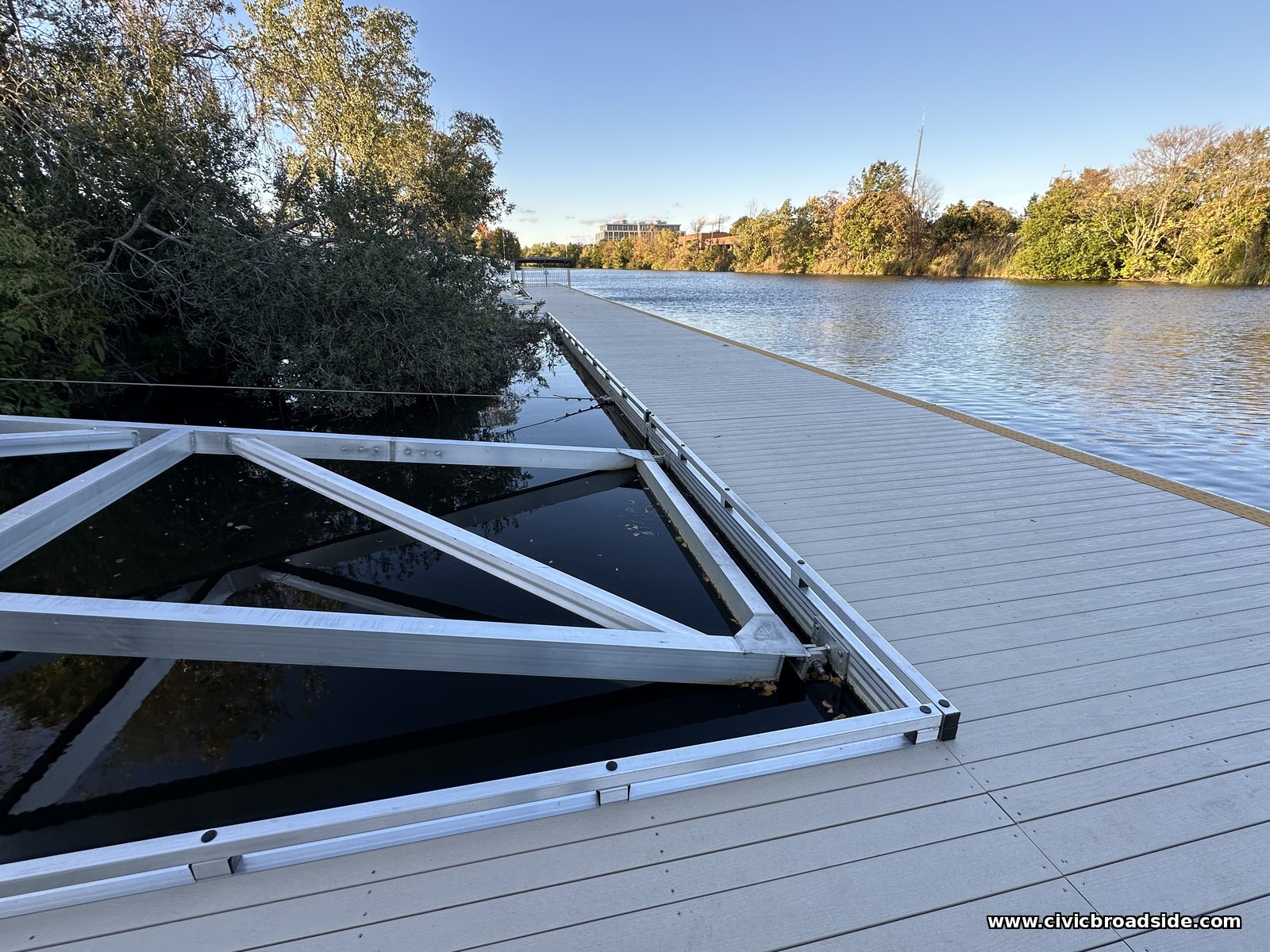 Pale dock decking beside an open aluminum triangular frame with dark river water visible through it