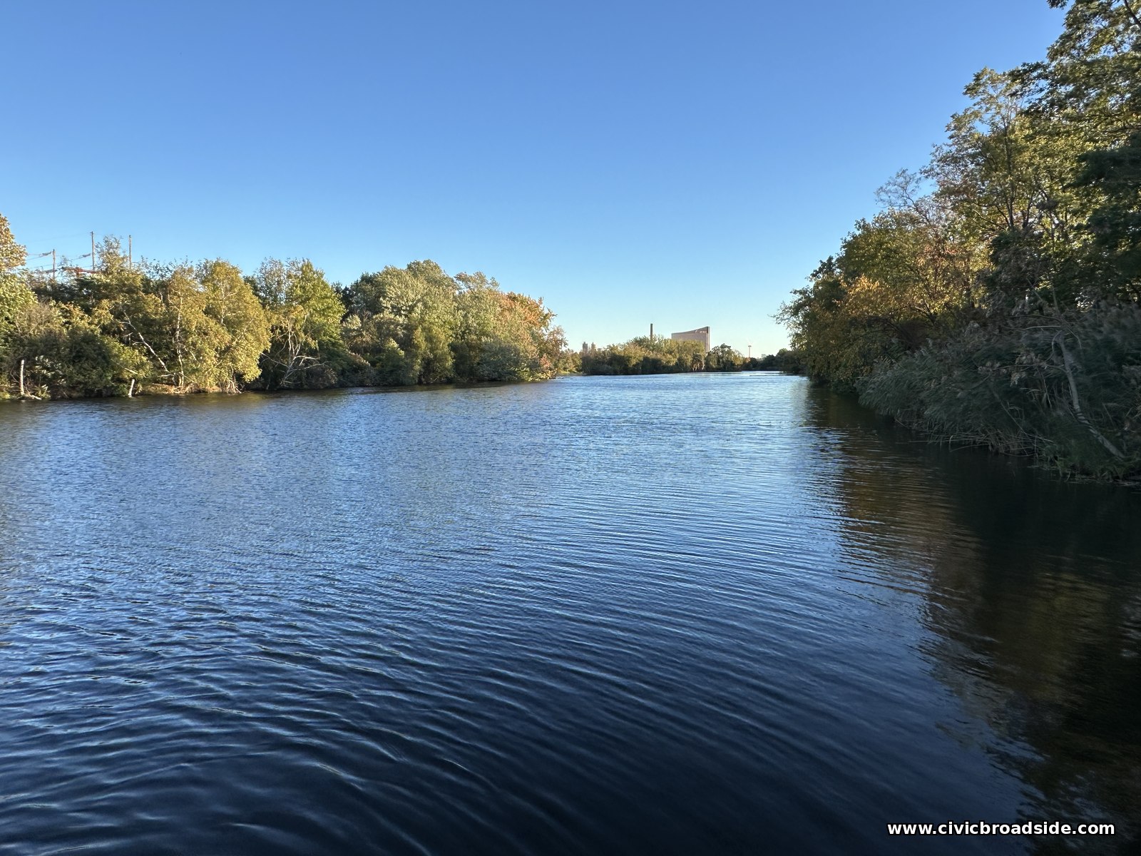 The Malden River in blue evening light, rippled by wind, with trees along both banks and a distant skyline