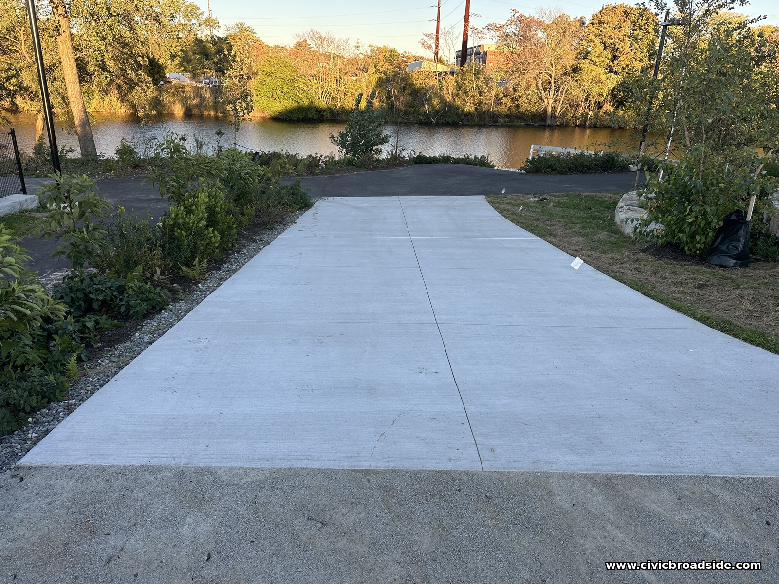 A smooth concrete ramp sloping toward the river between plantings, with the water visible at the far end